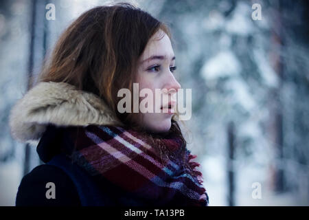 Una bella ragazza pallido con un rossore sulle sue guancie dal gelo si erge nel freddo inverno meteo nella foresta. Foto Stock