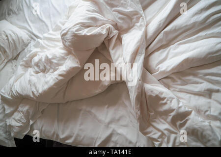 Letto comodo con lenzuola bianche in disordine. Cuscino bianco con coperta sul letto disfatto. Concetto di relax dopo mattina Foto Stock