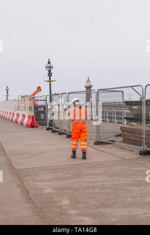 Riparazioni in corso sul molo a Whitby,North Yorkshire, Inghilterra,UK.Un lavoratore in tuta arancione passeggiate lungo il molo. Foto Stock