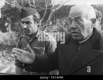 Un cattolico sacerdote spagnolo in un nero soutane e rivestire (destra) racconta soldati spagnoli qualcosa con gli occhi aperti. Sulla sinistra, un soldato francese di Franco, le truppe (con un cappuccio Gorillo). Foto Stock