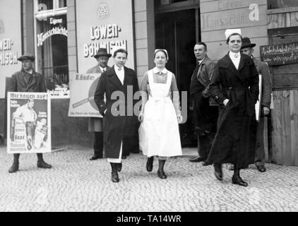 Gli infermieri del 'Marienheim' casa di riposo di lasciare la stazione di polling in 59 Chausseestrasse in occasione del Landtag prussiano elezione. Due sostenitori della campagna per le loro parti con manifesti elettorali. Il socialismo nazionale pubblicizza con il dire "Costruiamo!' Foto Stock