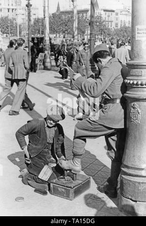 Un cittadino spagnolo soldato consente un uomo pulire le sue scarpe, mentre egli è la lettura di un quotidiano, nella parte anteriore di una lanterna sulla Rambla (passeggiata nel centro) in Barcellona, ??Catalogna, Spagna nel marzo del 1939, dopo la conquista di Barcellona dal generale Francisco Franco nel gennaio 1939. In background, flaneurs e soldati. Sulla lanterna, una chiamata di Franco per gli abitanti di Barcellona. Giù di sotto in ghisa a lanterna, lo stemma di Barcellona. Foto Stock