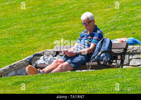 Lyme Regis, Dorset, Regno Unito. 21 maggio 2019. Regno Unito Meteo. Un uomo di crogiolarvi al sole in Lister giardini presso la stazione balneare di Lyme Regis in Dorset come egli gode di una calda giornata di sole. Credito Foto: Graham Hunt/Alamy Live News Foto Stock