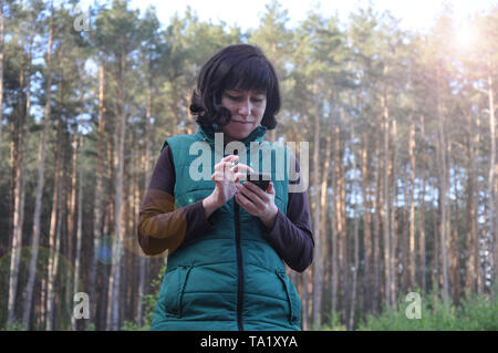 Bella giovane donna. freneticamente cercando nel telefono al di fuori della foresta Foto Stock