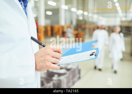 Le mani di una persona in camice bianco rendono una voce in una cartella con documenti in un magazzino. Contabilizzazione delle merci in magazzino. Foto Stock