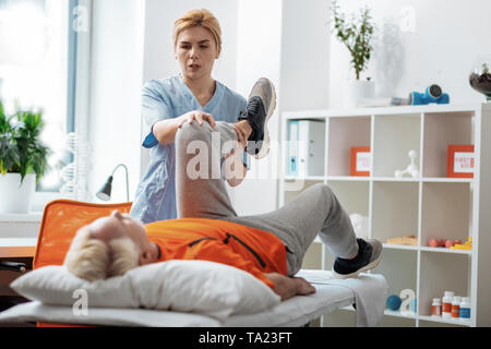 Bella donna bionda tenendo la sua gamba pazienti Foto Stock