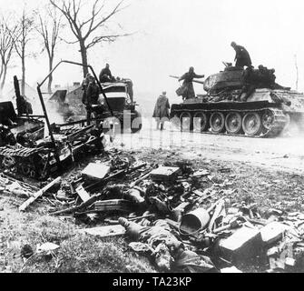 Russo T-34 serbatoio a Berlino. La Seconda Guerra Mondiale La Battaglia di Berlino nel 1945. L'anello difensivo attorno alla capitale imperiale è collassato. I serbatoi dell'Armata Rossa avanzare verso la città, passando dai morti soldati tedeschi e rovinato le posizioni difensive. Foto Stock