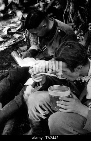 I soldati tedeschi si prendono una pausa per leggere il loro campo post e mangiare. Foto di Propaganda Company (PK): corrispondente di guerra Schuerer. Foto Stock