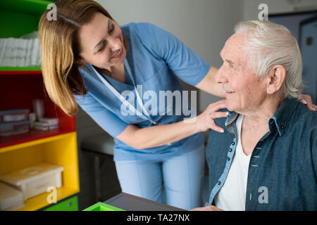 Felice Custode assiste senior l'uomo. Amichevole supporto infermiere uomo vecchio con il morbo di Parkinson Foto Stock