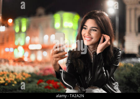 Donna scegliendo i brani sullo smartphone, a piedi di notte Foto Stock