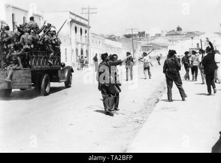 Foto di truppe in marcia attraverso la città di Aznalcollar, a nord-ovest di Siviglia, nell'estate del 1936. Sulla sinistra, un carrello trasporta giubilanti soldati spagnoli. Sulla destra, volontari in abiti civili e soldati della Guardia Civil, paramilitare unità di polizia che hanno aderito alla putschists quasi senza eccezione nel 1936. Foto Stock