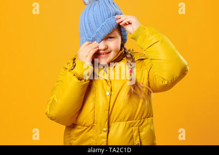 Closeup ritratto di un allegro bambina in camicia su sfondo giallo. Il Bambino guarda fuori da sotto il cappello. Foto Stock