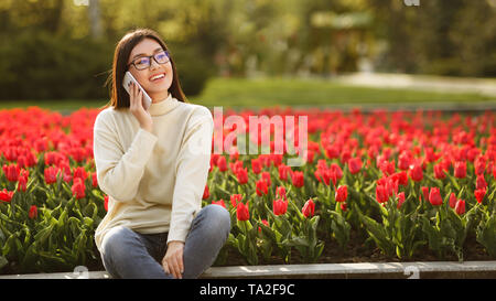 Felice ragazza parlando al telefono vicino tulipani rossi Foto Stock