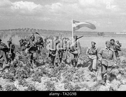 Foto di non regolare nazionale spagnolo di truppe marciando attraverso un campo della Meseta spagnola negli ultimi giorni della guerra il 28 marzo 1939. I soldati portano il loro intero campo pack e Spagnolo bandiere nazionali (rosso-giallo-rosso). In primo piano, un tenente (con un bastone e una sigaretta) è leader di truppe. In background, alberi di olivo. Foto Stock