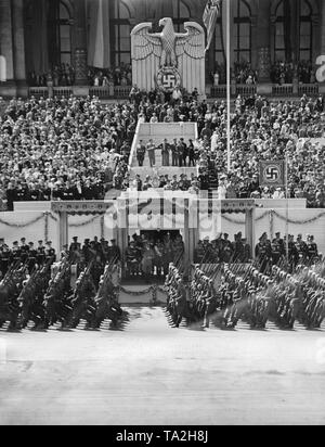 Foto del VIP stand durante la sfilata per la Legione Condor sull'asse est-ovest (ex Chalottenburger Chaussee, oggi Strasse des 17. Juni) davanti alla facciata principale della Technische Universitaet di Berlino del giugno 6th, 1939. Adolf Hitler (sotto una tettoia) sta dando la marching soldati il saluto nazista. Al centro sotto la Reichsadler (Imperial Eagle) con una croce uncinata, un commentatore radio. Foto Stock