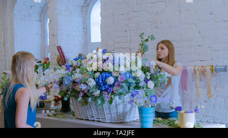 Due donne fioristi rendendo grande cesto floreale con fiori al negozio di fiori Foto Stock