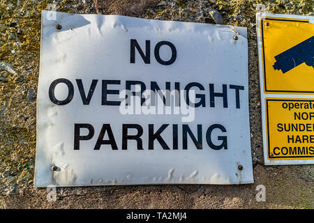 Parcheggio segno di restrizione con nessun parcheggio notturno scritto su di esso. A nord del porto di Sunderland, Seahouses, Northumberland, Regno Unito. Foto Stock