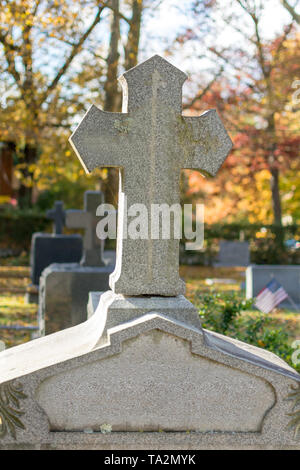 Una croce di pietra sulla cima di un camuffati lapide di granito a Sleepy Hollow cimitero su un calmo e tranquillo pomeriggio autunnale Foto Stock