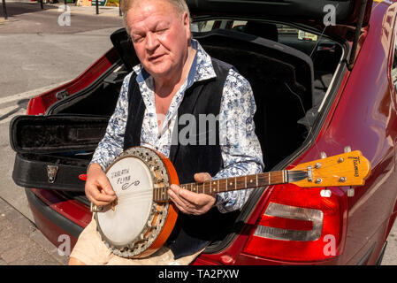 Ritratto di Jarlath Flynn - il conducente locale di taxi flamboyant seduto nel bagagliaio della sua auto e giocando un banjo mentre si aspettano le tariffe al taxi stand BHZ Foto Stock