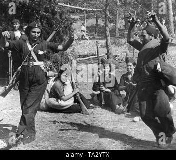 Foto di due danze combattenti repubblicano dietro la linea del fronte in Sierra Peguerinos a nord-ovest di Madrid. Il ballerino di sinistra è vestito in generale e è armato con un Gewehr 98 del fucile. Indossa la chevron di Teniente (tenente) sul suo cappuccio. Il suo partner di ballo riproduce le nacchere e indossa un mantello e porta un sacco. In background, combattenti e combattenti femmina guarda divertito. Foto Stock