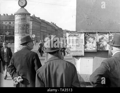 I passanti da osservare il giornale visualizza a Odeonsplatz a Monaco di Baviera. Sul lato anteriore della pagina dei Münchner Abendblatts è segnalato: 'l'avanzamento continua'. Il 'Illustrierte Beobachter' in scena sulla sua pagina anteriore di un armonioso scena familiare con la madre e il bambino. Foto Stock