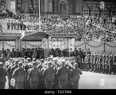 Foto del VIP stand durante la sfilata per la Legione Condor sull'asse est-ovest (ex Chalottenburger Chaussee, oggi Strasse des 17. Juni) davanti alla facciata principale della Technische Universitaet di Berlino del giugno 6th, 1939. Adolf Hitler (sotto una tettoia) sta dando la marching soldati il saluto nazista. A sinistra sotto la Reichsadler (Imperial Eagle) con una croce uncinata, un commentatore radio. La banda musicale della Wehrmacht è in riproduzione. Foto Stock