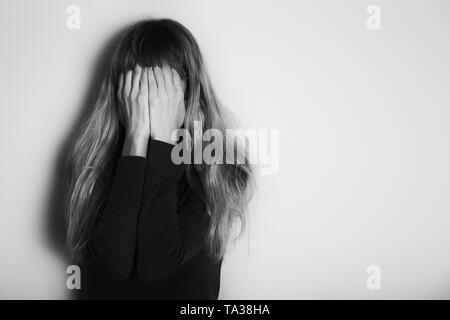 Premuto donna in piedi da solo nella parte anteriore della parete.intenzionalmente immagine in bianco e nero. Foto Stock