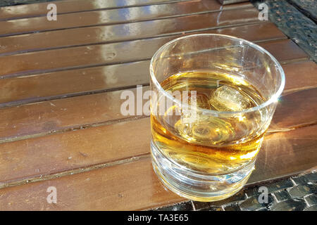 Bicchiere di whiskey su ghiaccio con bottiglia sul tavolo di legno Foto Stock