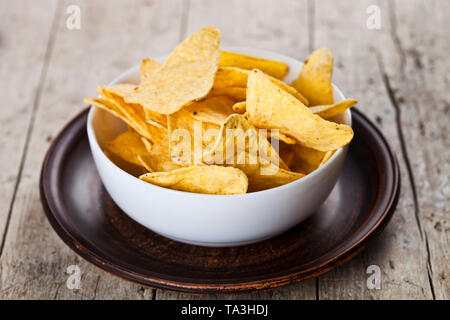 Mexican nachos chips in ciotola bianco su marrone piastra ceramica. Rustico in pietra in legno sfondo. Foto Stock