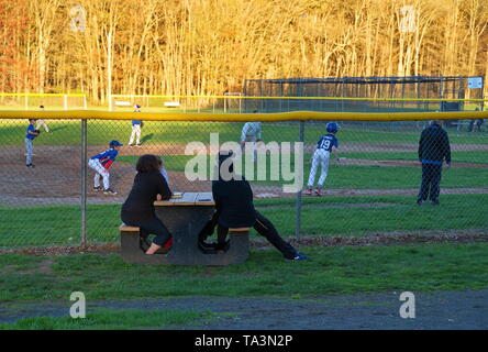 Di middelmark CT, Stati Uniti d'America. Apr 2019. I genitori a guardare i loro bambini a giocare a baseball su un bel pomeriggio in un parco locale. Foto Stock