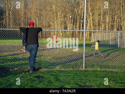 Di middelmark CT, Stati Uniti d'America. Apr 2019. Papà guardando il suo figlio a baseball pratica da al di fuori del recinto su una bella nuova Inghilterra pomeriggio. Foto Stock