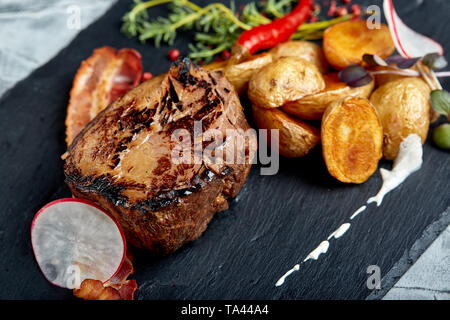 Bistecca di manzo servito con patate al forno e verdura,sfondo nero, close-up. concept food. Foto Stock