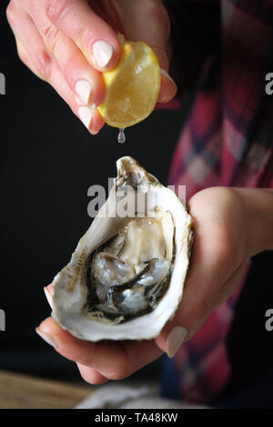 Donna spremendo il succo di limone sulle materie oyster, primo piano Foto Stock
