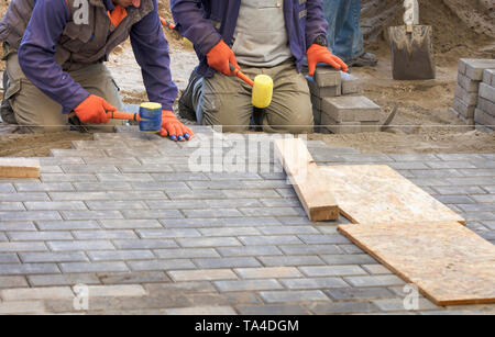 I lavoratori appoggiare la lastra di pavimentazione con speciali martelli, livellamento secondo il livello del filo teso Foto Stock
