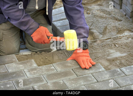 Il lavoratore appoggiare la lastra di pavimentazione con speciali martelli, livellamento secondo il livello del filo teso Foto Stock