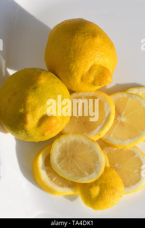 Intero e limoni a fettine sul piatto bianco Foto Stock