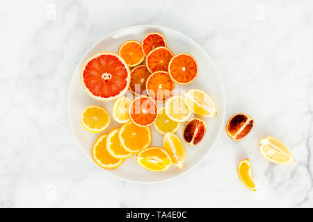 Disposizione di tagliare le arance arance pigmentate, limone e pompelmo su un grande piatto bianco e marmo bianco dello sfondo. Vista dall'alto. Foto Stock