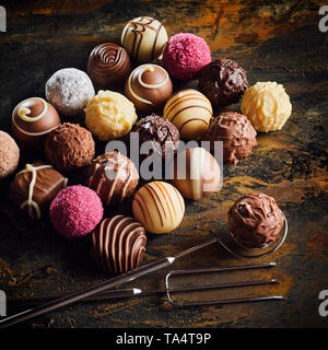 Presentazione di lusso cioccolato artigianale bomboni in assortimento di motivi decorativi disposti ordinatamente su un rustico o vintage tavolo in legno con filo e forcella Foto Stock