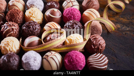 Assortimento di gourmet specialità artigianali praline di cioccolato con twirled festoso nastro per una celebrazione o dono nel panorama formato banner Foto Stock