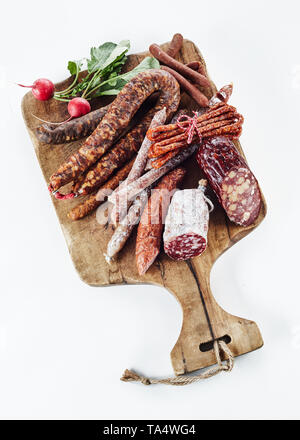 Selezione di regionale tedesco piccante di salsicce e salami servita su un vecchio tagliere di legno con un fresco e ravanelli per uno spuntino isolati su whi Foto Stock