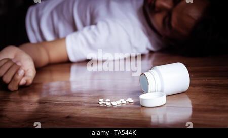 Depressione uomo suicidarsi da sovradosaggi sul farmaco. close up di overdose di pillole di plastica dal contenitore della medicina con premere l'uomo sul piano Foto Stock
