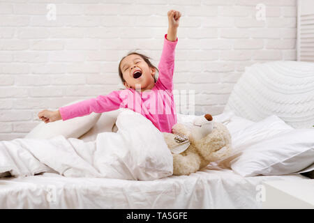 Grazioso fanciullo ragazza si risveglia dal sonno e sbadigli nel letto la mattina Foto Stock