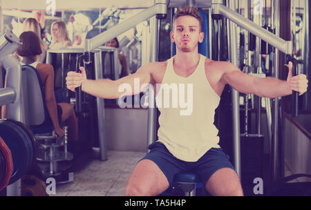 Giovane spagnolo ben addestrato uomo utilizzando pec deck palestra macchine in ambienti chiusi Foto Stock