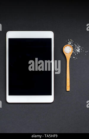 Lay piatto vista aerea tablet PC gadget mockup vuoto lo spazio di testo su sfondo nero con un cucchiaio di sale. Menu design blog alimentare ricetta cookbook o consegna copie Foto Stock