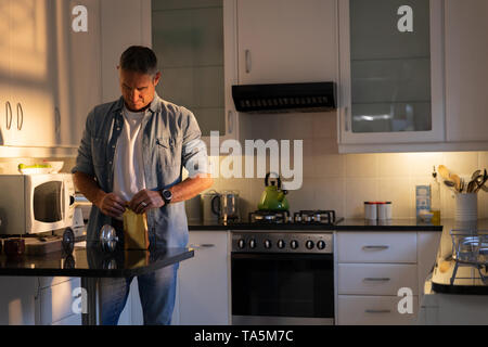 Uomo maturo di apertura busta di carta di caffè in cucina Foto Stock