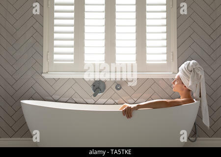 Premurosa donna seduta nella vasca nella stanza da bagno Foto Stock