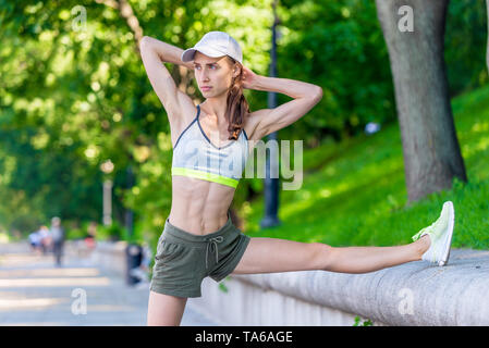 Slanciata donna atletica in fase di riscaldamento prima di fare jogging in un parco della città Foto Stock