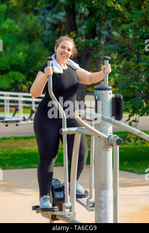 Ritratto di un giovane attivo grasso donna impegnata su un simulatore di passo a passo in un parco Foto Stock