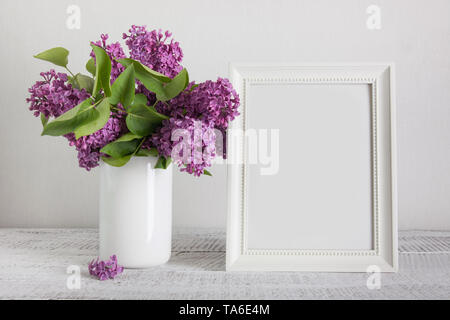 White photo frame e sentori di viola lilla fiori in vaso. Spazio per il testo. Vintage. Festa della mamma mock up. Foto Stock