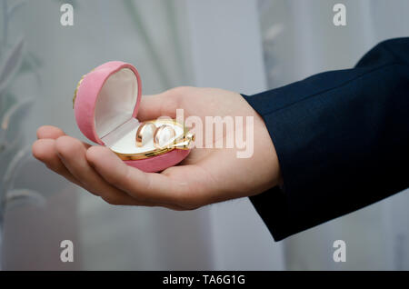 In velluto rosa scatola con anelli di nozze nella mano dello sposo che il giorno del matrimonio Foto Stock